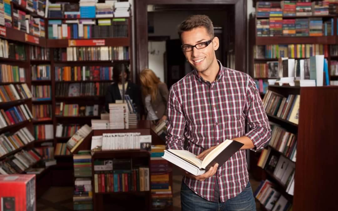 Man with glasses smiling and reading a book.